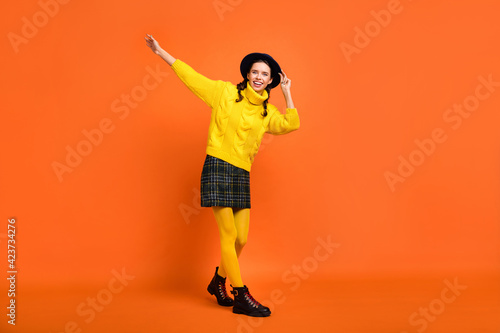 Full size photo of optimistic girl dance go wear yellow sweater cap skirt shoes isolated on orange background