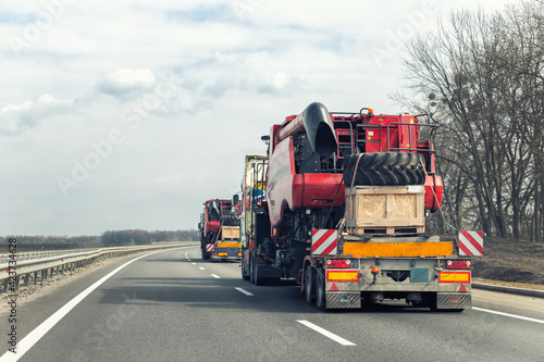 Many heavy industrial truck with semi trailer platform transport disassembled combine harvester machine on common highway road on sunset or sunrise day. Agricultural equipment transportation service