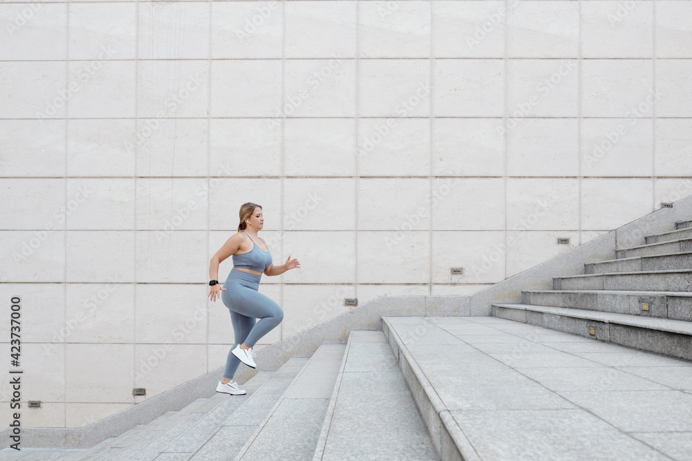 Determined fit plus size young woman running up the stairs outdoors, training in city and reaching the goal concept
