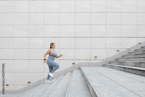 Determined fit plus size young woman running up the stairs outdoors, training in city and reaching the goal concept © DragonImages