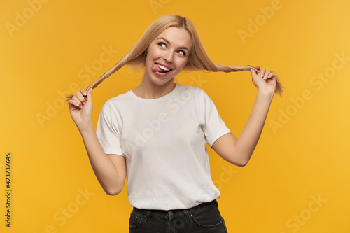 Nice looking woman, beautiful girl with long blond hair. Wearing white t-shirt and black jeans. hold her hair and smiling broadly. Watching at the camera, isolated over orange background
