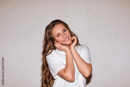 Teen girl with long curly hair and make up posing near the wall with copy space