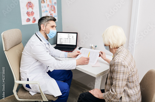 Doctor wearing in medical mask consults a senior woman on the results of a cardiogram and tests. Diagnostic heart diseases, heart attacks, and tachycardia in the elderly photo