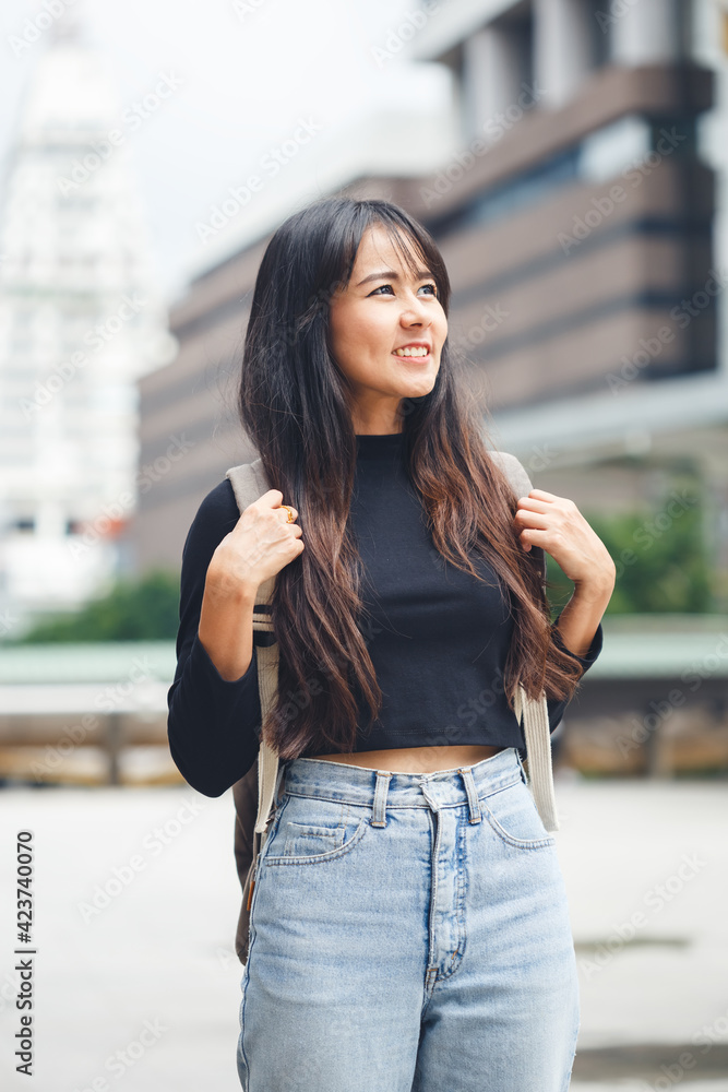 Portrait of asian young woman with backpack standing in city center.