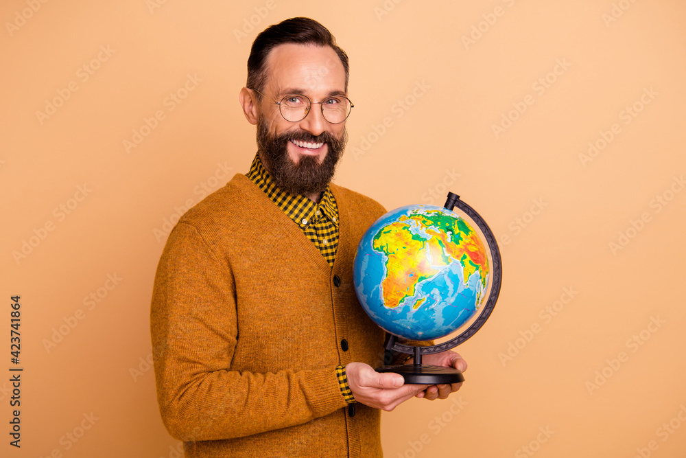 Photo of positive mature man teacher hold globe wear sweater isolated over beige color background Photo of positive mature man teacher hold globe wear sweater isolated over beige color background