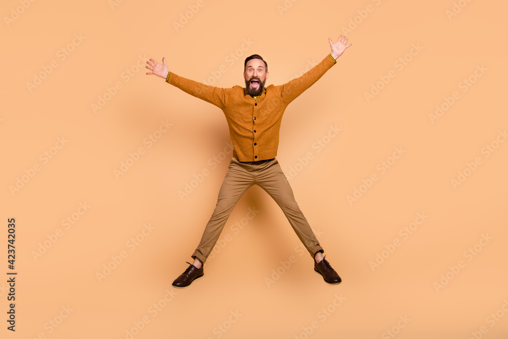 Full size photo of optimistic brown hair man jump wear brown sweater pants shoes isolated on beige color background