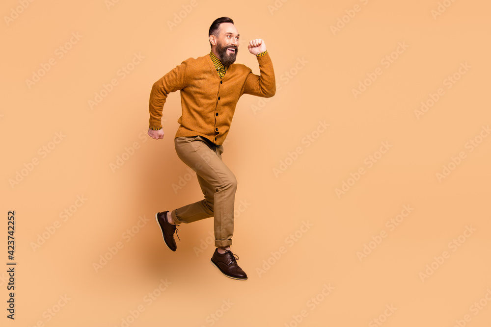 Full size profile photo of optimistic brown hair man jump wear brown sweater pants shoes isolated on beige color background