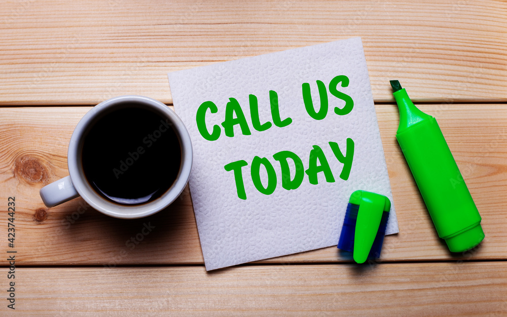 On a wooden table, a cup of coffee, a green marker and a napkin with the text CALL US TODAY On a wooden table, a cup of coffee, a green marker and a napkin with the text CALL US TODAY