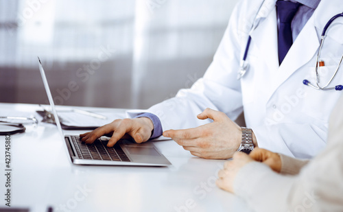 Unknown male doctor and patient woman discussing something while sitting in clinic and using laptop. Best medical service in hospital, medicine, pandemic stop