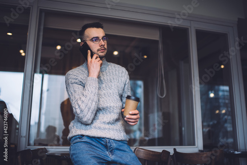 Focused man talking on phone and holding cup of beverage