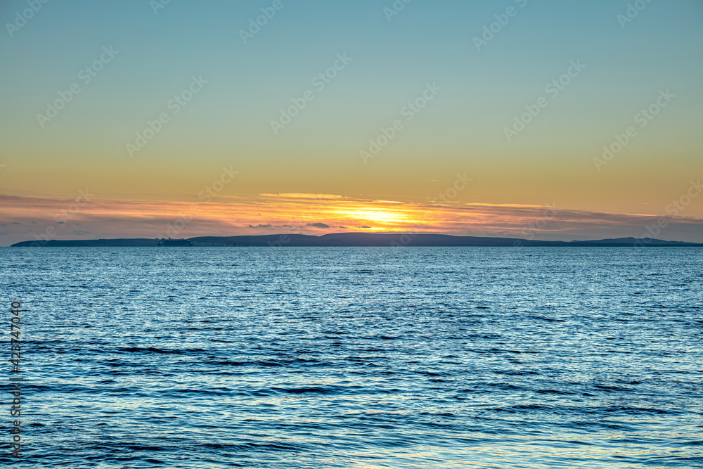 A beautiful sunset over a choppy blue sea and hills in the background under a majestic blue sky