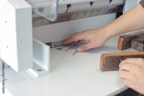 a specialist operator removes the scraps and edges of a stack of business cards or tags on an automatic paper cutting machine, a professional cutter, equipment for a printing house or workshop.