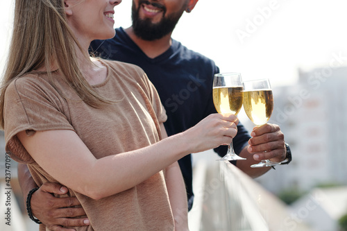 Cropped image of smiling hugging young couple enjoying drinking champagne on rooftop