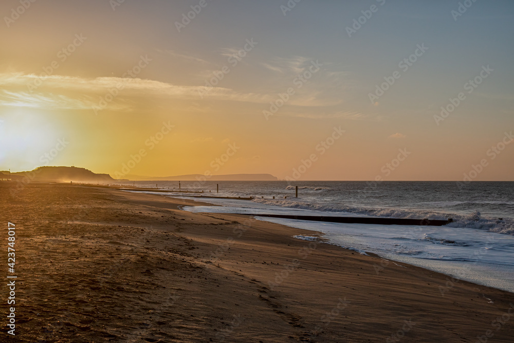A beautiful sunrise at a sandy beach with choppy sea and wooden groyne (breakwater) under a majestic blue sky