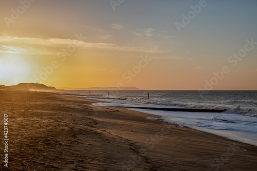 A beautiful sunrise at a sandy beach with choppy sea and wooden groyne (breakwater) under a majestic blue sky