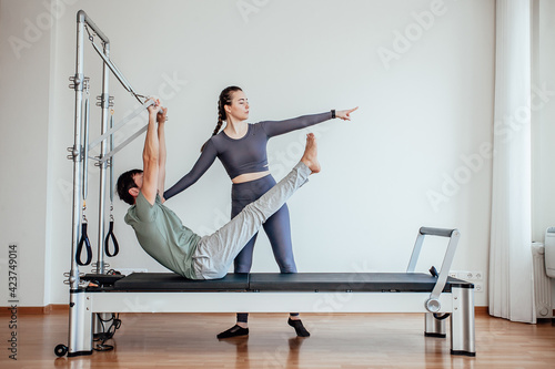 Reformer Pilates. An attractive man working out with a pilates instructor in the gym
 photo