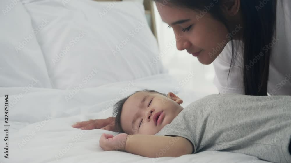 Young asian mother kiss cheek of little baby girl with tender on bed in the bedroom, mom love newborn and care, mother with expression with child together, parent and daughter, family concept. Young asian mother kiss cheek of little baby girl with tender on bed in the bedroom, mom love newborn and care, mother with expression with child together, parent and daughter, family concept.