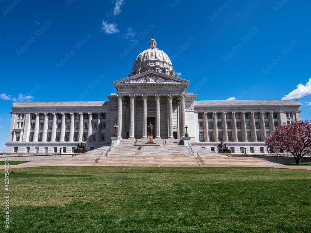 View of front entrance to Missouri State Capitol building that houses Missouri General Assembly and executive branch of government with blue sky and grass foreground in spring