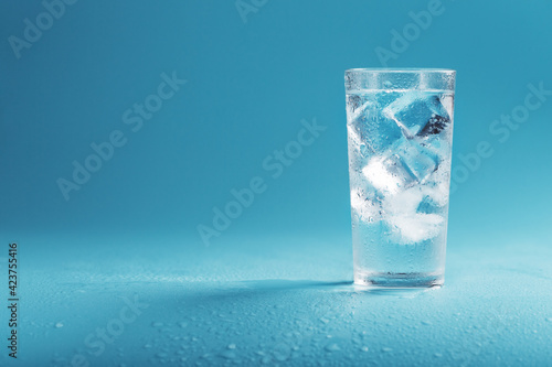 A glass with ice water and ice cubes on a blue background.