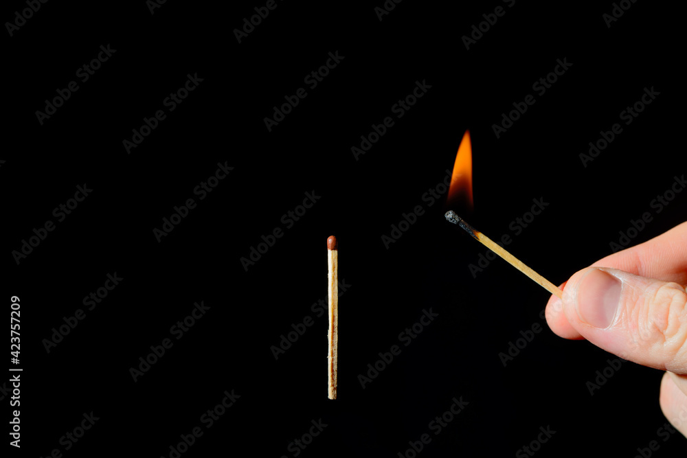 burning match in his hand ignites a second match on a black background burning match in his hand ignites a second match on a black background