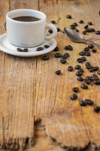 Top view of white cup of coffee, on rustic wooden table with coffee beans and spoon, selective focus, vertical, with copy space