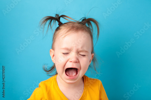 Photo Upset little baby girl crying on blue background. Top view