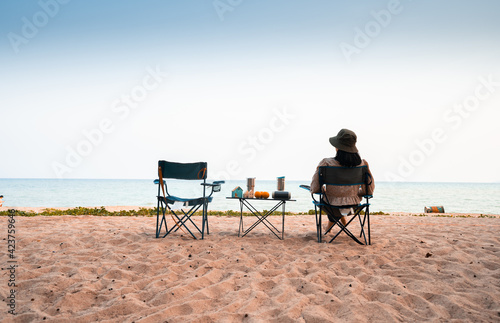 Asian female tourists sit on beach chairs, tables with orange speakers, glasses and house models, and one empty chair.
