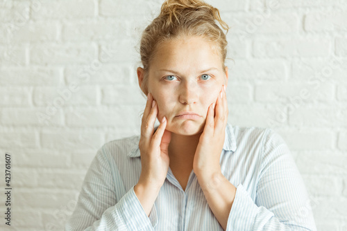 Photos Close up serious upset woman touching her face with two hands while looking at the camera