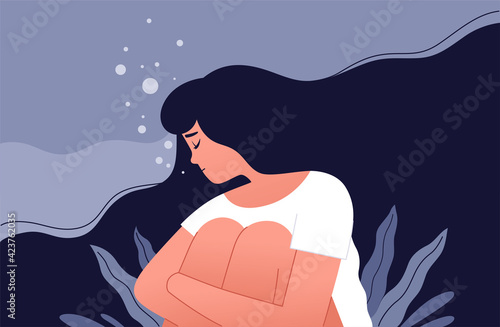 The unhappy girl sits and hugs her knees in a sea of her own sorrow. Sad lonely woman in depression with flying hair. Concept of a person trapped in the bottom due to stress photo