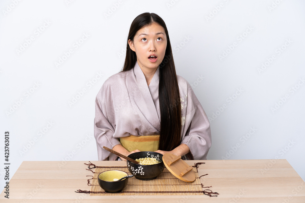 Young Chinese girl wearing kimono and eating noodles looking up and with surprised expression Young Chinese girl wearing kimono and eating noodles looking up and with surprised expression