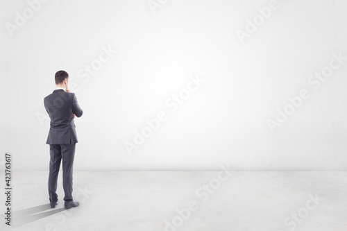 Thinking about future concept with businessman in empty room with blank light wall with copyspace for your text. Mock up photo