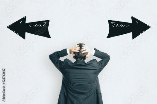 Fotografía Choice concept with businessman grabbing his head looking at white wall with handwritten black opposite looking arrows