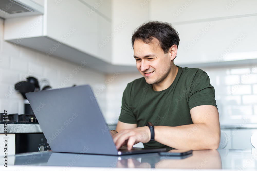 Handsome man using a laptop in the kitchen. Working from home in quarantine lockdown. Social distancing Self Isolation Handsome man using a laptop in the kitchen. Working from home in quarantine lockdown. Social distancing Self Isolation