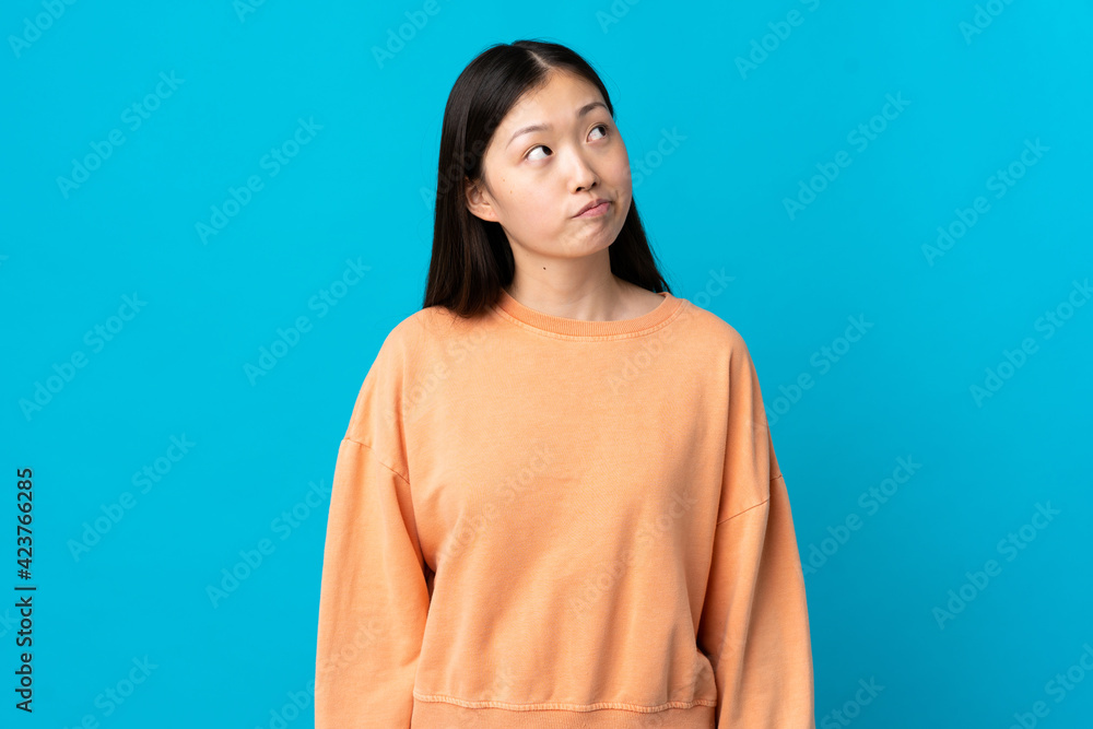 Young Chinese girl over isolated blue background and looking up Young Chinese girl over isolated blue background and looking up