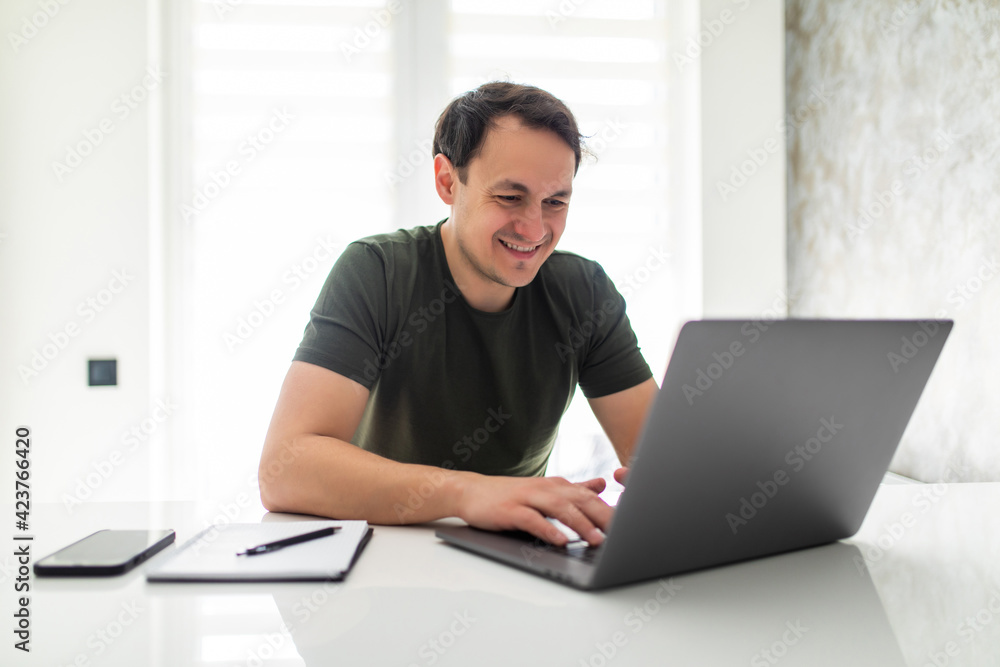 Handsome young man calculating domestic bills or taxes, household expenses, managing budget, paperwork, checking financial documents, using laptop in modern kitchen Handsome young man calculating domestic bills or taxes, household expenses, managing budget, paperwork, checking financial documents, using laptop in modern kitchen