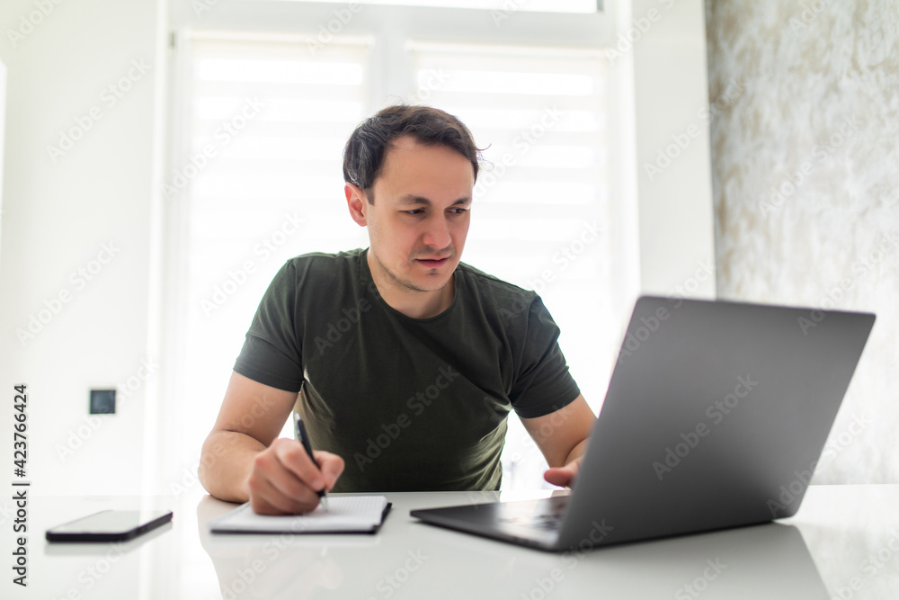 Handsome young man calculating domestic bills or taxes, household expenses, managing budget, paperwork, checking financial documents, using laptop in modern kitchen Handsome young man calculating domestic bills or taxes, household expenses, managing budget, paperwork, checking financial documents, using laptop in modern kitchen