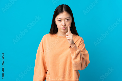 Young Chinese girl over isolated blue background frustrated and pointing to the front