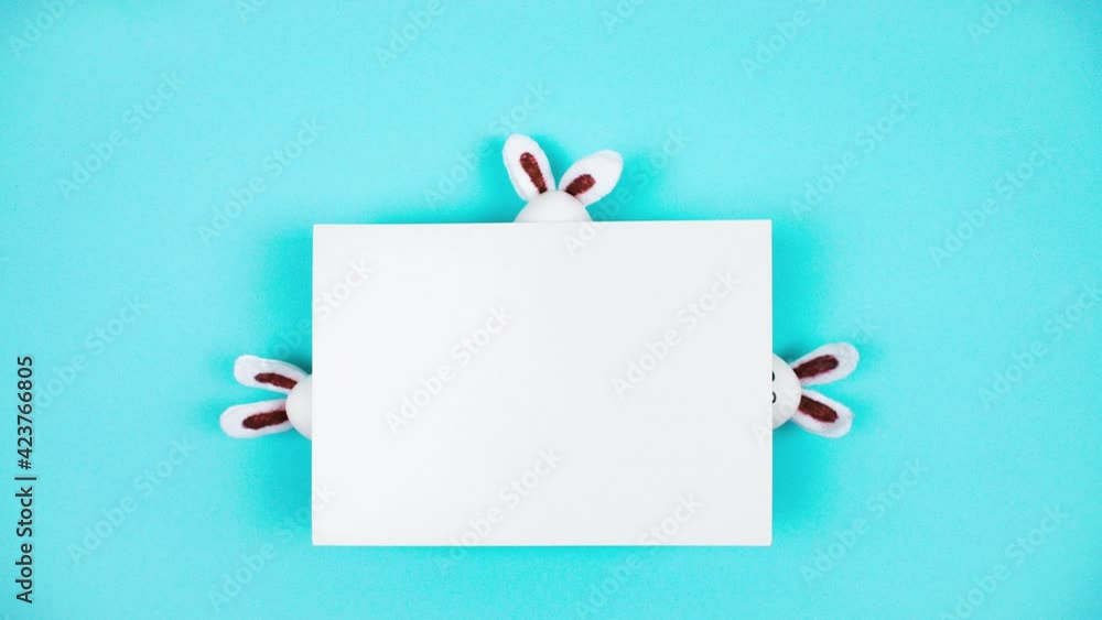 4k Three white eggs and three Easter bunnies appear and hide behind a sheet of white paper. Happy Easter Day Concept. Light blue background. Template for text. Stop motion animation. Copy space. 4k Three white eggs and three Easter bunnies appear and hide behind a sheet of white paper. Happy Easter Day Concept. Light blue background. Template for text. Stop motion animation. Copy space.