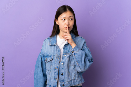 Young Chinese girl over isolated purple background showing a sign of silence gesture putting finger in mouth