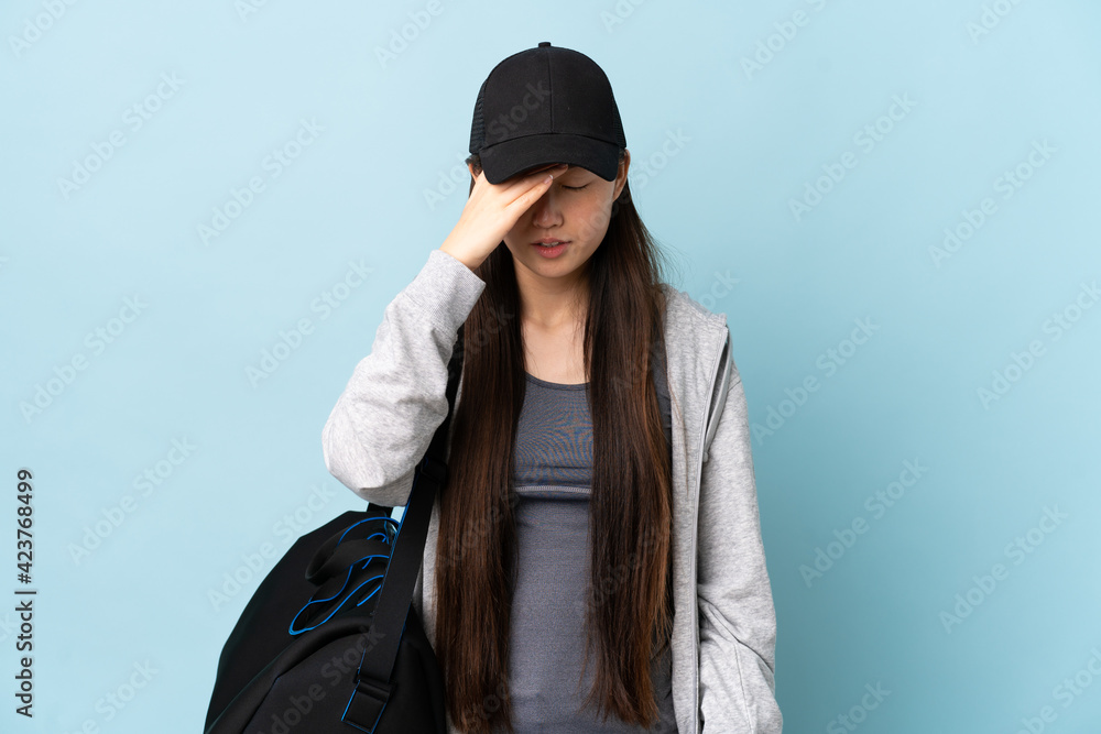 Young sport Chinese woman with sport bag over isolated blue background with headache Young sport Chinese woman with sport bag over isolated blue background with headache