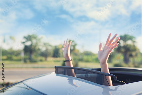 woman putting his hands out of the car sunroof top, driving down a country road photo