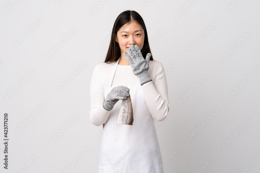 Chinese fishmonger wearing an apron and holding a raw fish over isolated white background happy and smiling covering mouth with hand Chinese fishmonger wearing an apron and holding a raw fish over isolated white background happy and smiling covering mouth with hand