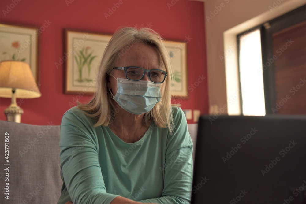 A woman sits in front of her laptop at home, talking with colleagues on a video call and watching content online
