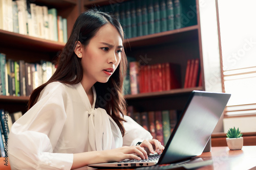 Candid of young attractive Asian woman working having trouble on her laptop computer working late at night.