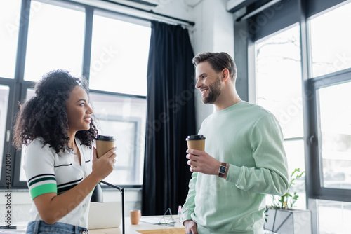 positive interracial coworkers talking in office while holding paper cups