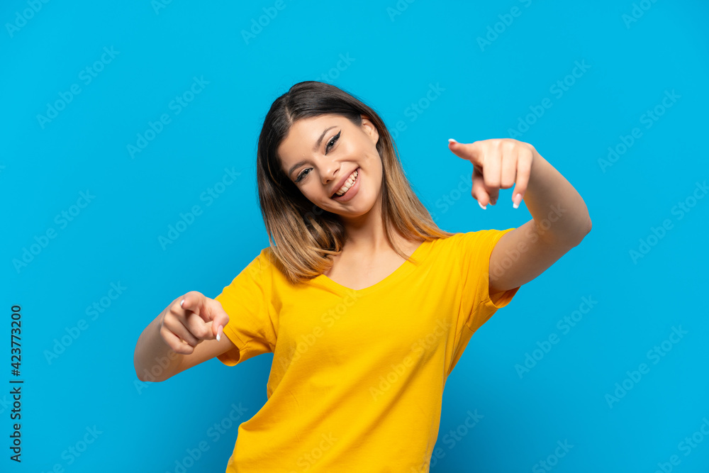Young Russian girl isolated on blue background pointing front with happy expression Young Russian girl isolated on blue background pointing front with happy expression