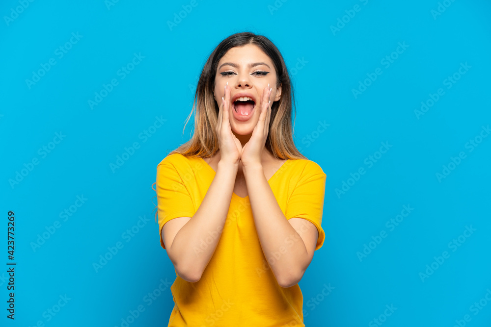 Young Russian girl isolated on blue background shouting and announcing something Young Russian girl isolated on blue background shouting and announcing something