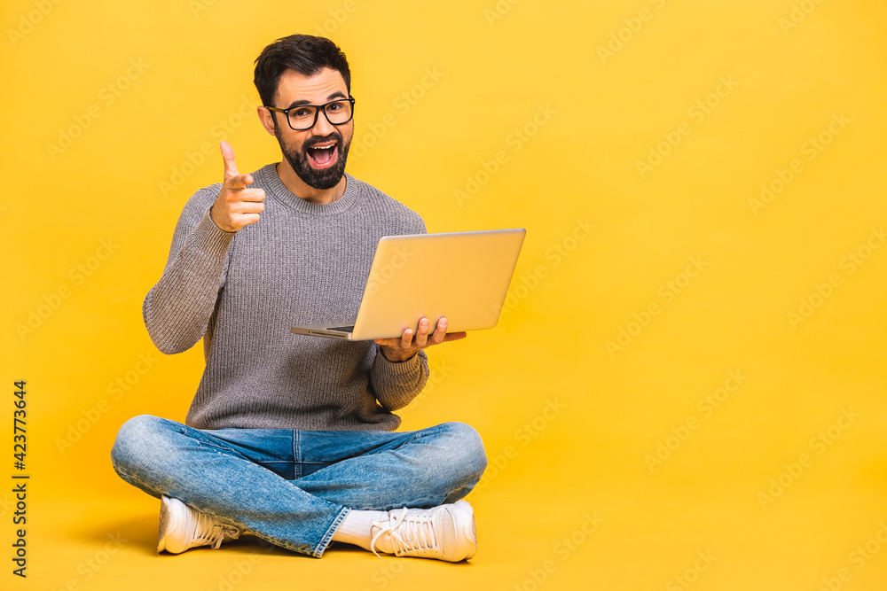 Successful winner! Portrait of a happy young bearded man using laptop and celebrating success or victory isolated over yellow background. Successful winner! Portrait of a happy young bearded man using laptop and celebrating success or victory isolated over yellow background.
