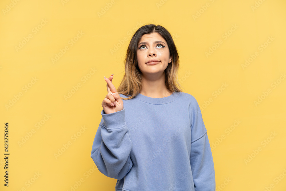 Young Russian girl isolated on yellow background with fingers crossing and wishing the best Young Russian girl isolated on yellow background with fingers crossing and wishing the best