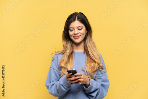 Young Russian girl isolated on yellow background sending a message with the mobile